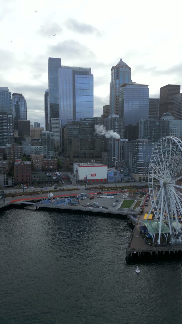 Vertical aerial drone shot of coastal, giant Ferris Wheel along downtown city skyline during overcast day - Seattle Great Wheel, Washington, USA