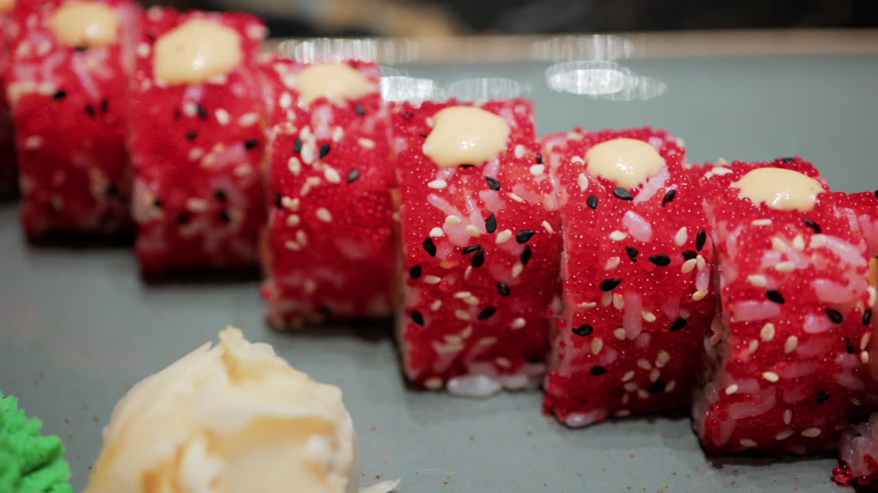 Close up of vibrant red sushi rolls topped with creamy sauce and sesame seeds, served on a ceramic plate