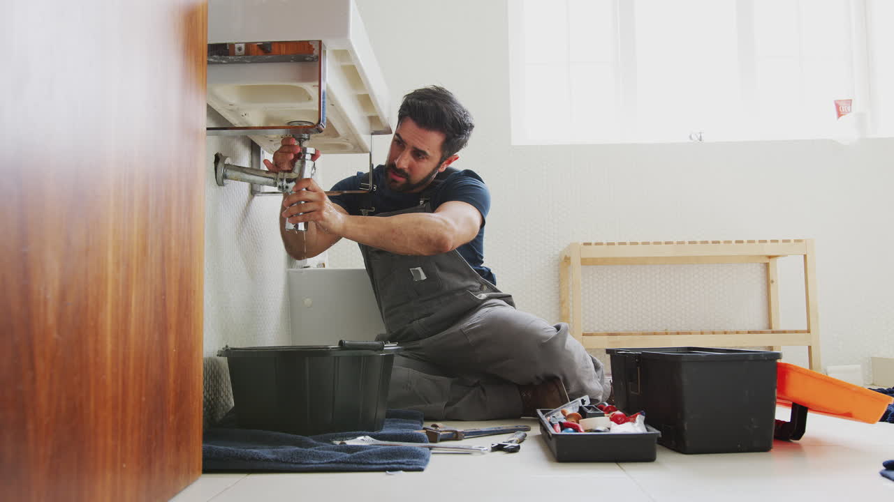 fontanero masculino trabajando para arreglar el fregadero con fugas en el baño de la casa