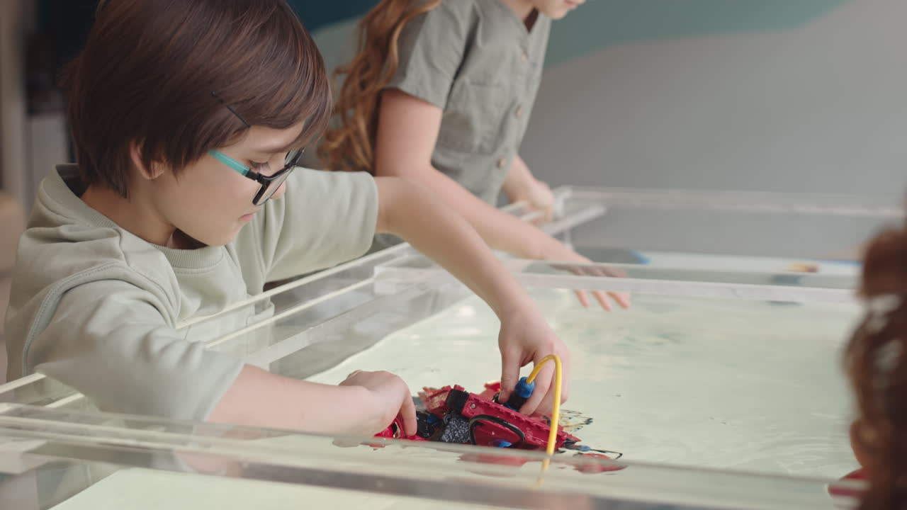 Three Caucasian Pupils Putting Robo Boat into Water