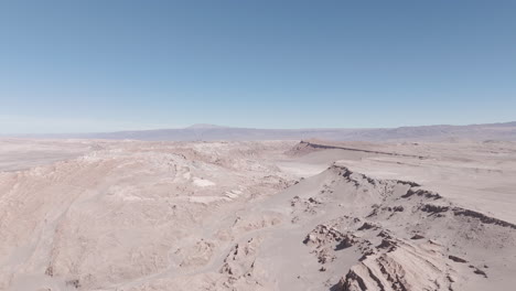 drone shot flying over the dry sand desert mountains in san pedro de atacama chile south america on a blue sky day near mars valley and valley de la luna log