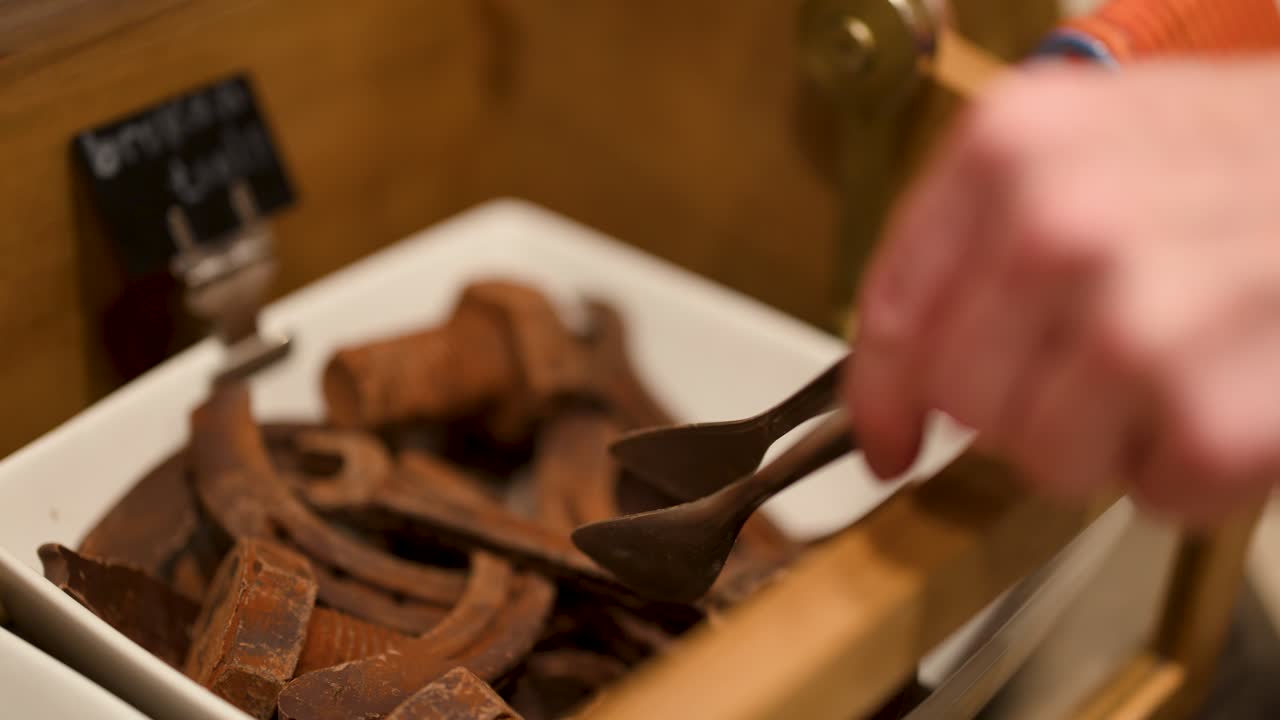 Hand uses tongs to pick chocolate wrench from display under warm, inviting shop lighting