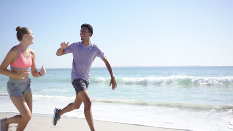 young caucasian woman and biracial man high-five on a sunny beach with copy space