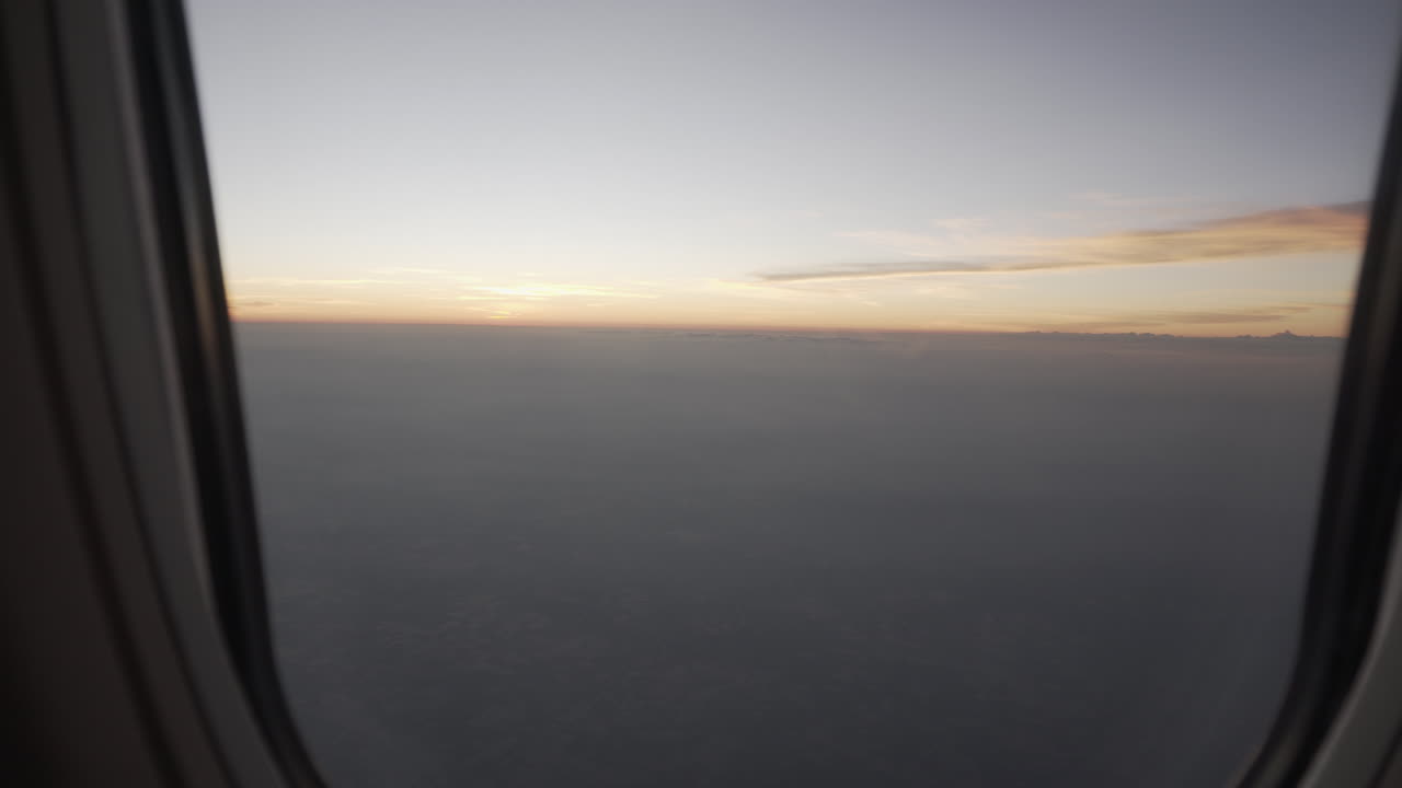 4K truck slide shot to the left and right of an airplane window from the inside revealing a beautiful view of the sunrise or sunset outside with low clouds and colorful sky.