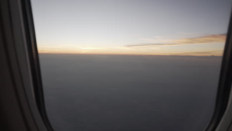 4k truck slide shot to the left and right of an airplane window from the inside revealing a beautiful view of the sunrise or sunset outside with low clouds and colorful sky.