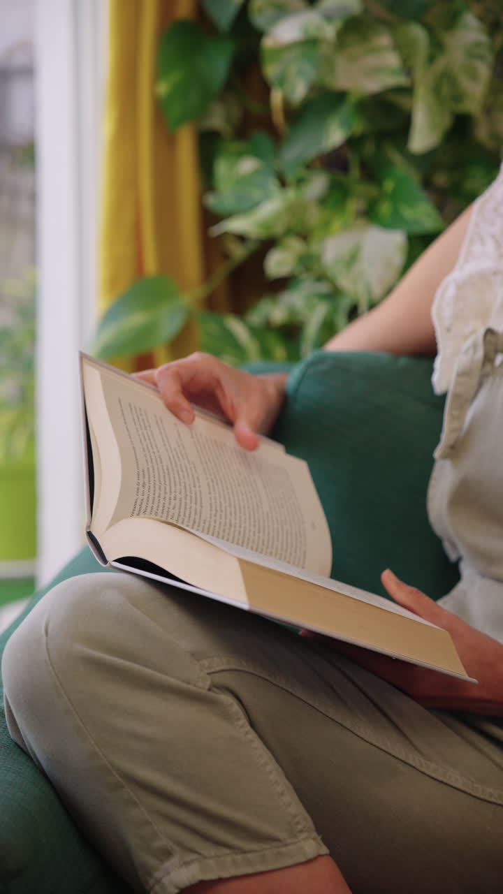 Primo piano di una donna che legge un libro e gira una pagina a casa. Momento di vita tranquilla, svago e relax in un ambiente interno accogliente.