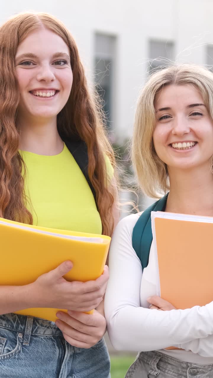 Two smiling female students holding books on a lively school campus