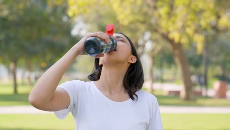 indian woman drinking water from a bottle sipper in a park in morning