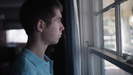 cinematic shot of a sad young teenage boy, high school aged young man with depression and anxiety looking out window sadly