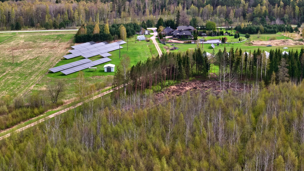 Aerial of rural property with solar panels, green fields, and expansive forest
