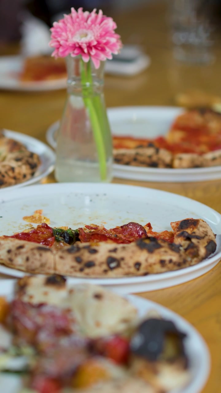 Una mano serve pizza ai peperoni su un piatto bianco durante una cena gourmet a un tavolo di legno di ristorante.