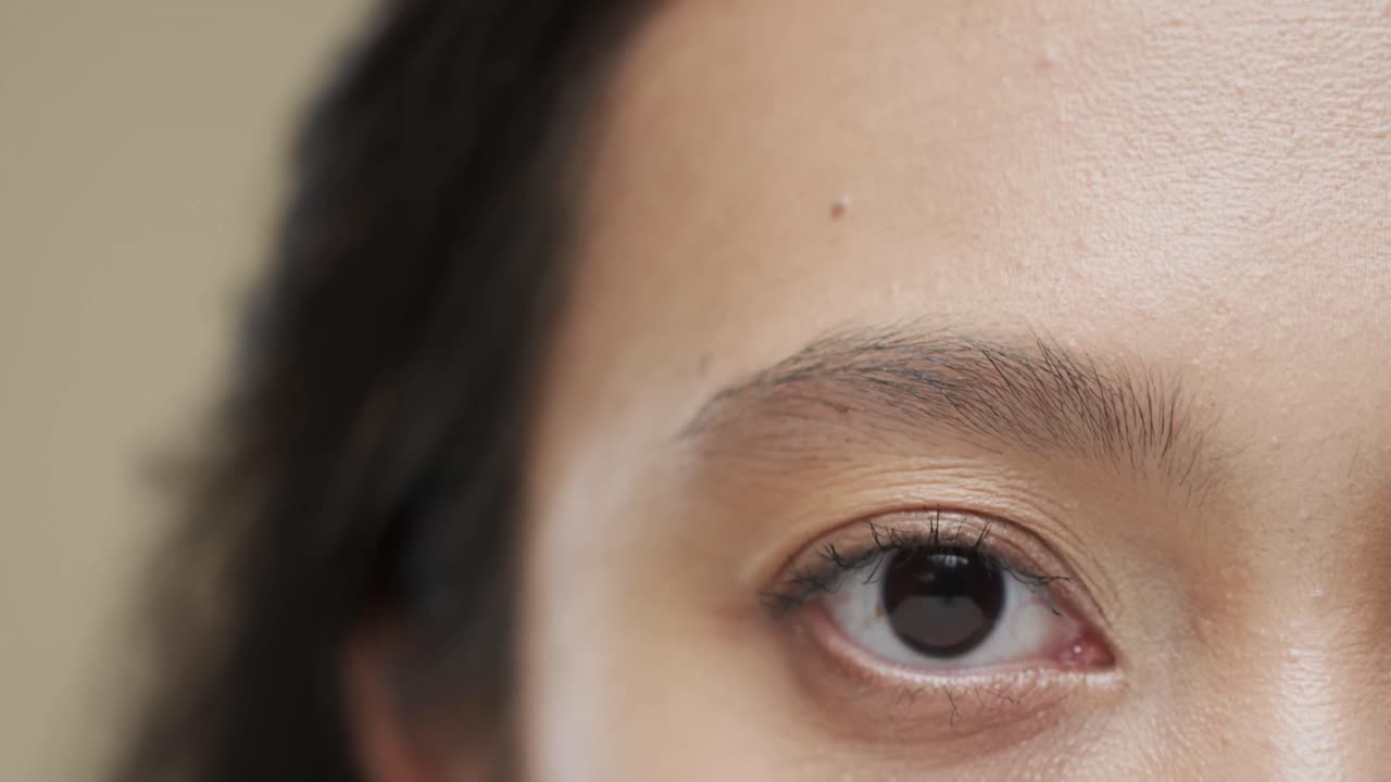 베이지색 배경에 어두운 머리카락을 가진 아시아 여성의 눈, 느린 동작