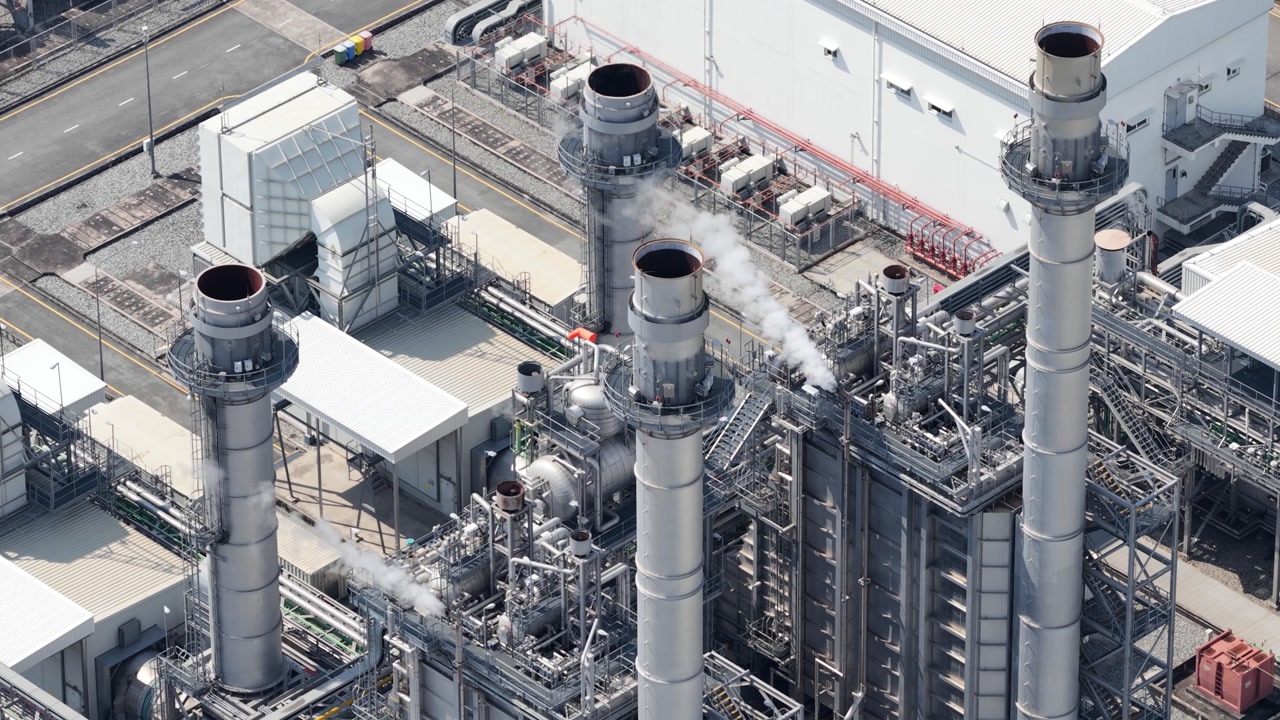 High angle perspective of a combined cycle power plant with its towering smokestacks releasing steam, illustrating the intricate infrastructure of modern energy and electricity generation