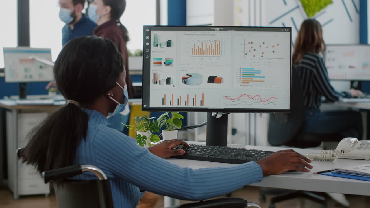 empleada africana inválida con máscara protectora comprobando informes en la computadora