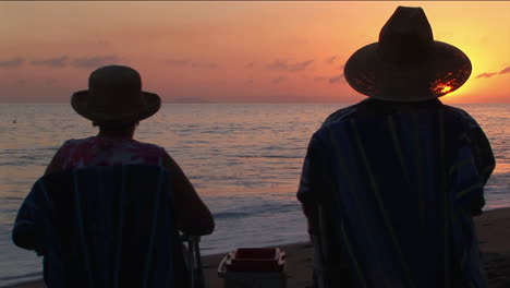 a couple toasts the ocean as they sit on a beach