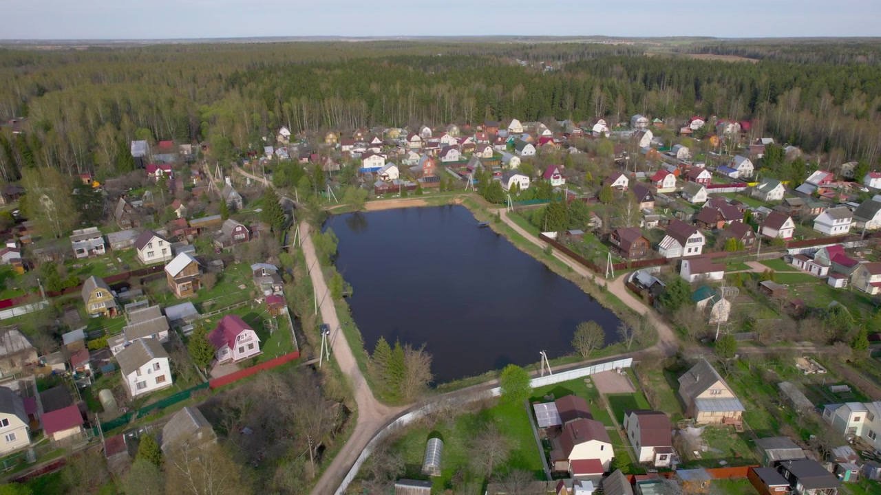 Widok z drona na wiejskie domy rozmieszczone wokół ciemnego kwadratowego stawu, z drogami, ogrodami i otaczającym lasem, dla tematyki nieruchomości wiejskich i planowania przestrzennego
