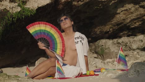 man relaxing on beach with pride flag and rainbow fan