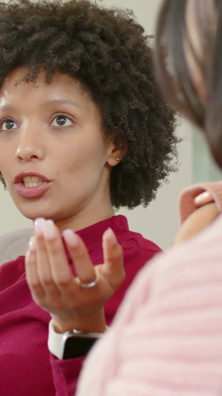 Vertical video: Replying after partner prompt, burgundy-top woman talking, gesturing at home, watch
