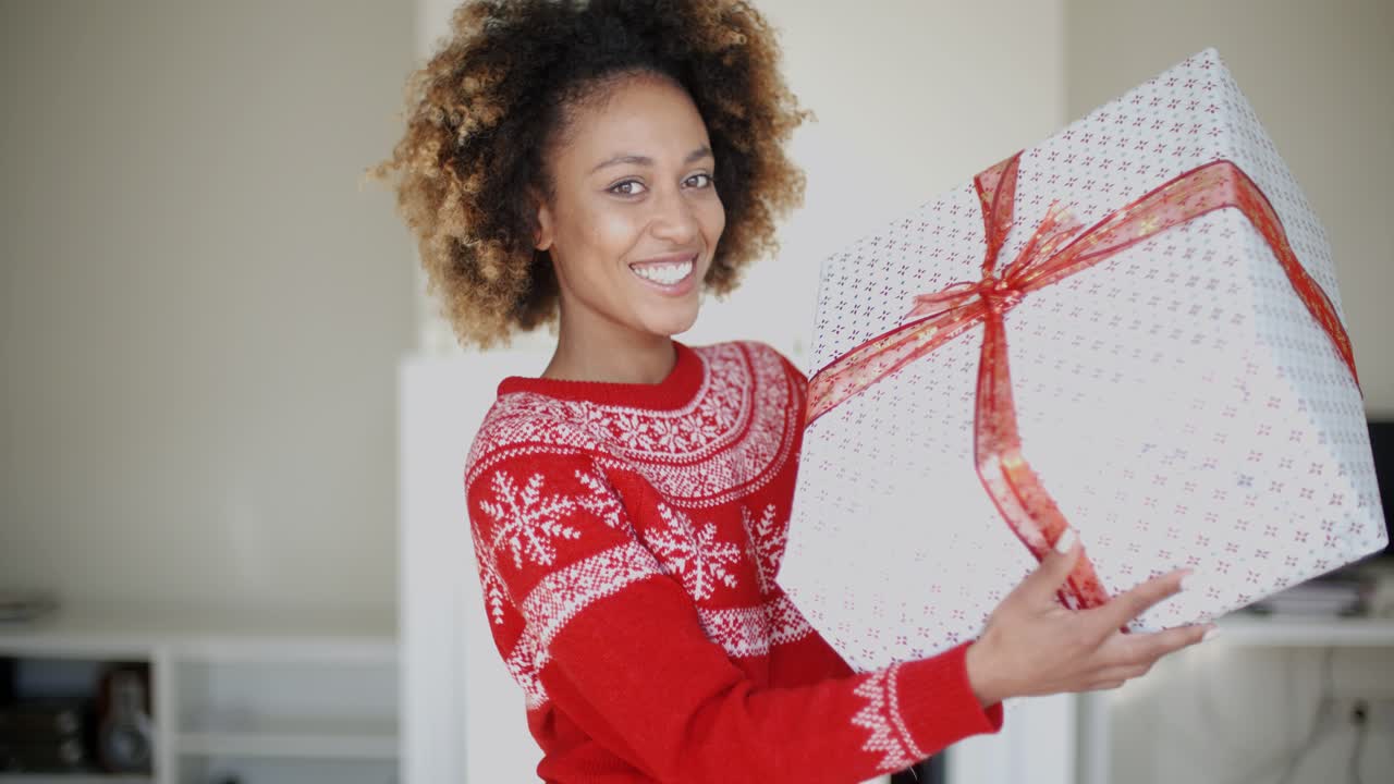 una chica feliz y sonriente con un corte de pelo afro sosteniendo un regalo