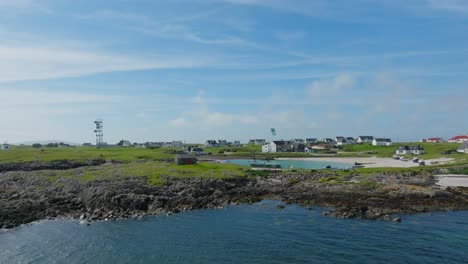 Fly-away-shot-of-harbour-next-to-a-village-with-a-person-kitesurfing-in-it,-on-the-Isle-of-Tiree