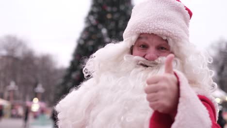 senior santa in a red coat shows thumbs up on the background of the christmas tree senior santa in a red coat shows thumbs up on the background of the christmas tree as a sign of the thumb up to take a picture on camera christmas and new year concept