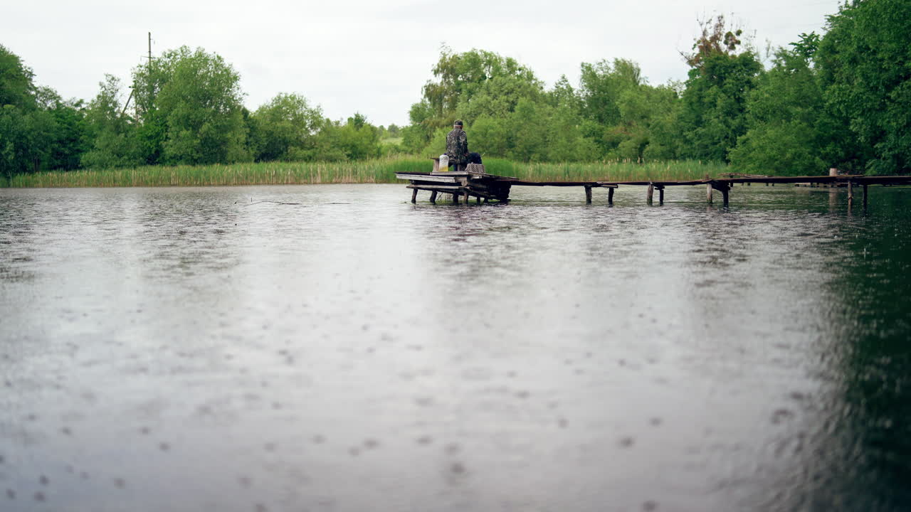 Fishing from dock on lake. Rear view of fisherman on the pier during rain