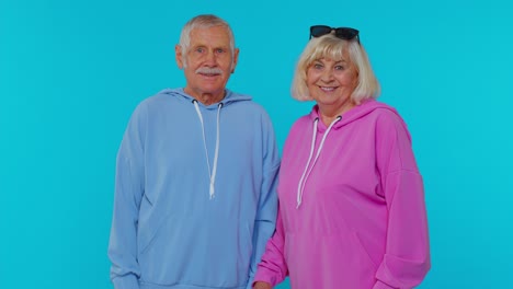 Senior-granny-with-grandfather-turning-and-smiling-at-camera-waving-hands-gesturing-hello-or-goodbye