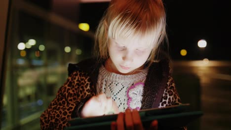 A-Girl-Enjoys-The-Tablet-On-The-Background-Of-A-Large-Window-With-Reflections