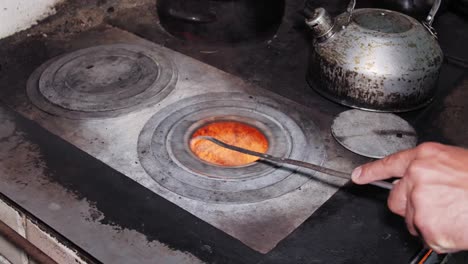 el hombre mueve las chimeneas con el póquer y coloca la tetera sucia en la estufa de la vieja cocina rústica