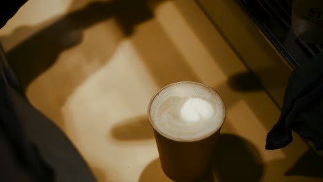 high angle detail shot of barista finishing a latte with heart shaped foam in the center - slow motion