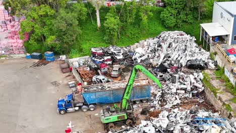 Aerial footage showing a scrapyard with green machinery sorting metal piles and parked trucks.