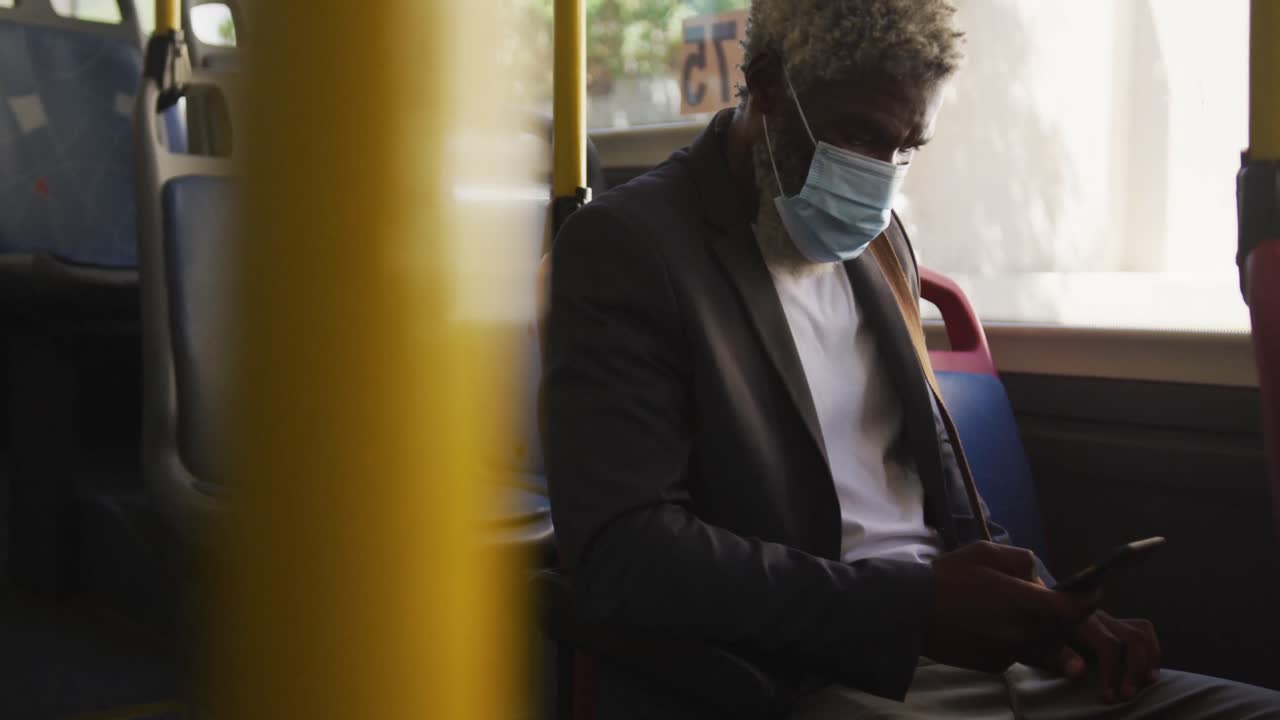 버스에 앉아 스마트 폰을 사용하는 얼굴 마스크를 쓰고 있는 아프리카계 미국인 노인