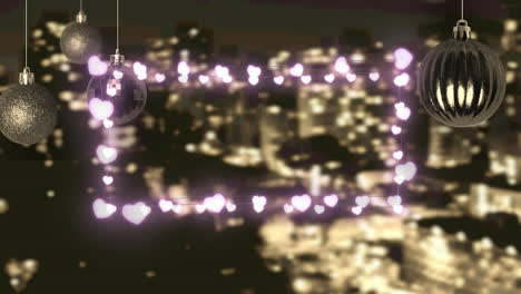 Pink-heart-shaped-fairy-lights-and-hanging-bauble-decorations-against-aerial-view-of-cityscape