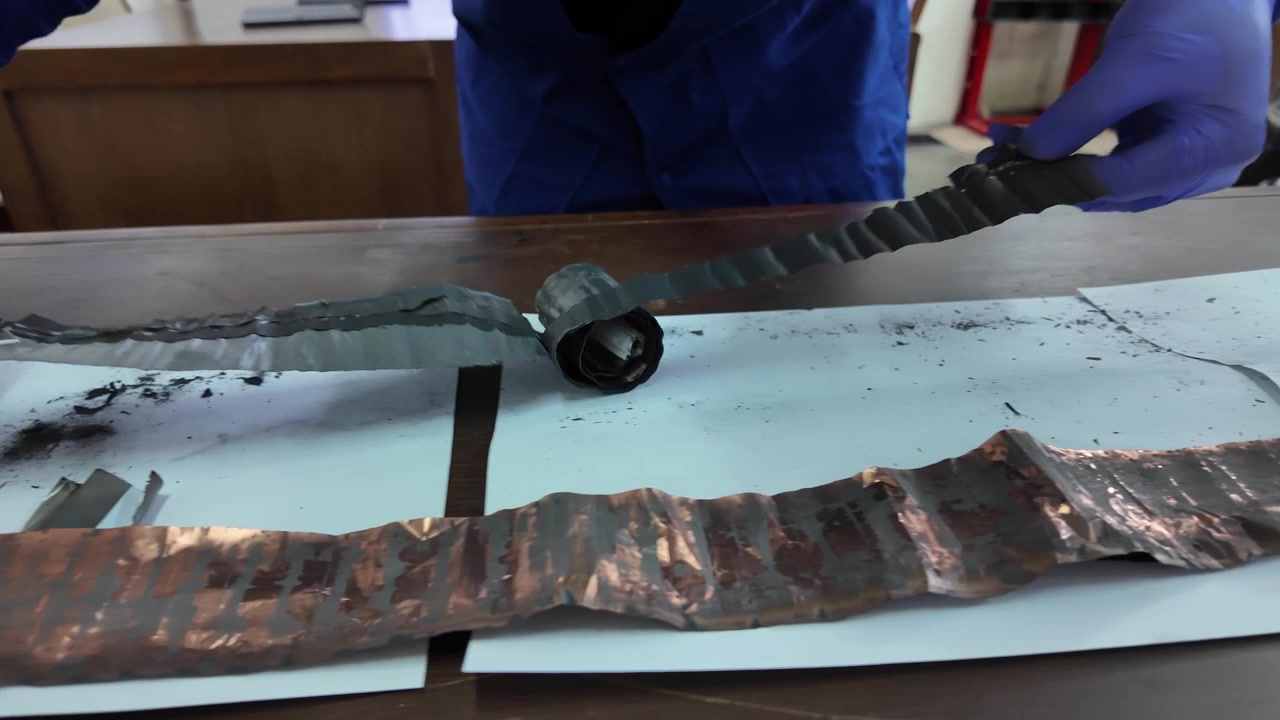 Un tecnico che indossa guanti protettivi blu smonta attentamente e srotola gli strati interni di una batteria agli ioni di litio