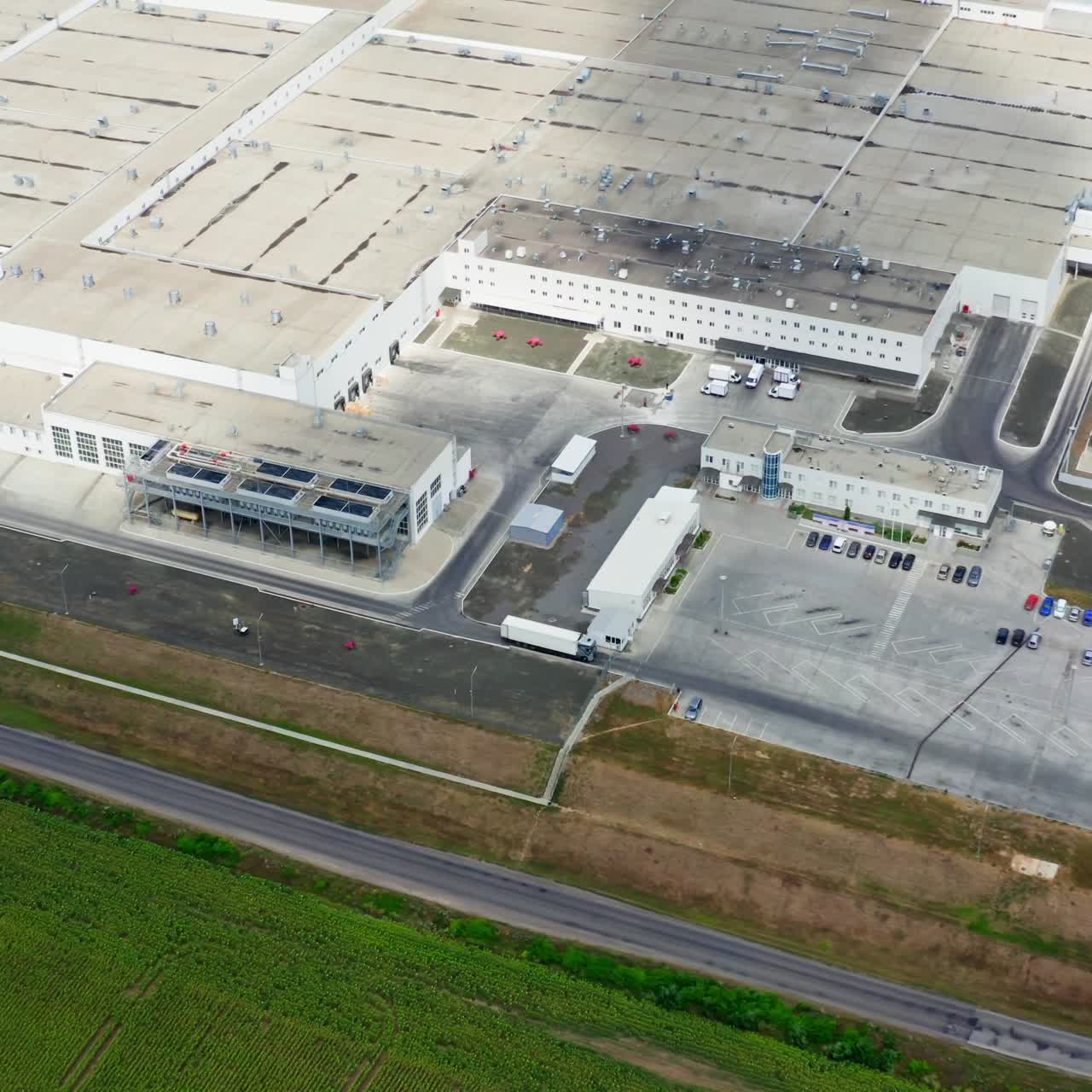 Huge industry near green field. Roofs of industrial buildings of a modern factory with car parking in summer. Top aeriel view