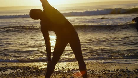 vista trasera de un surfista caucásico adulto estirándose y calentándose antes de surfear en la playa 4k
