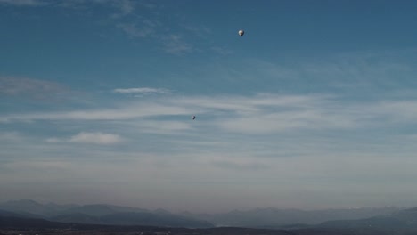 aerial shot of two tiny air balloons under a light cloudy sky