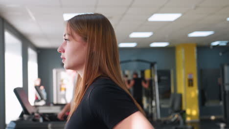 athletic woman jogging on treadmill in gym with two men running on adjacent machines and another person doing push ups in background under bright ceiling lights in spacious workout facility