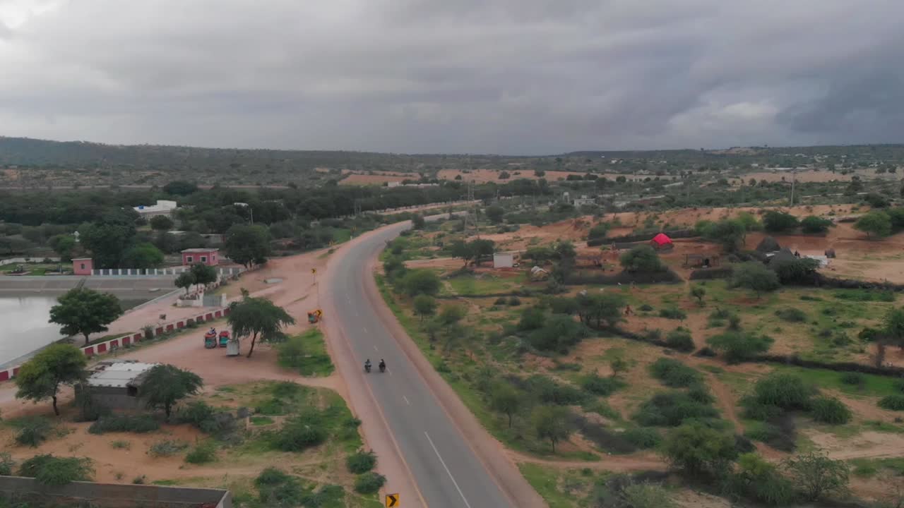 drone captura a dos motociclistas conduciendo su bicicleta en la carretera aislada de tharparkar que está rodeada de arena, hierba y arbustos
