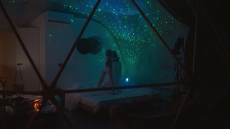 little girl plays and indulges with mother while jumping on bed in glamping bedroom. dimly lit room with bright projections of stars on white ceiling