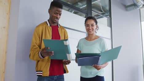 feliz diverso hombre y mujer colega creativo mirando documentos en carpetas y hablando