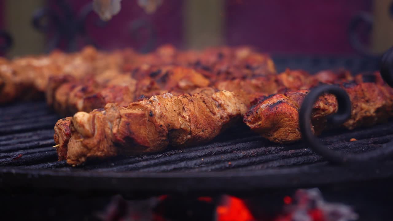 Carne grigliata allo spiedo che cuoce uniformemente sopra il fuoco in una bancarella di cibo all'aperto, vapore che sale al rallentatore