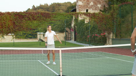 vista trasera de un hombre deportivo jugando al tenis con una mujer rubia en la cancha al aire libre en un día de verano