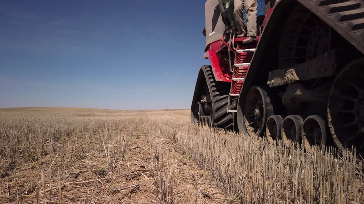 Giovane agricoltore caucasico con cappello scende le scale di un grande trattore rosso versatile su un terreno agricolo pianeggiante coltivato, Saskatchewan, Canada, primo piano statico.
