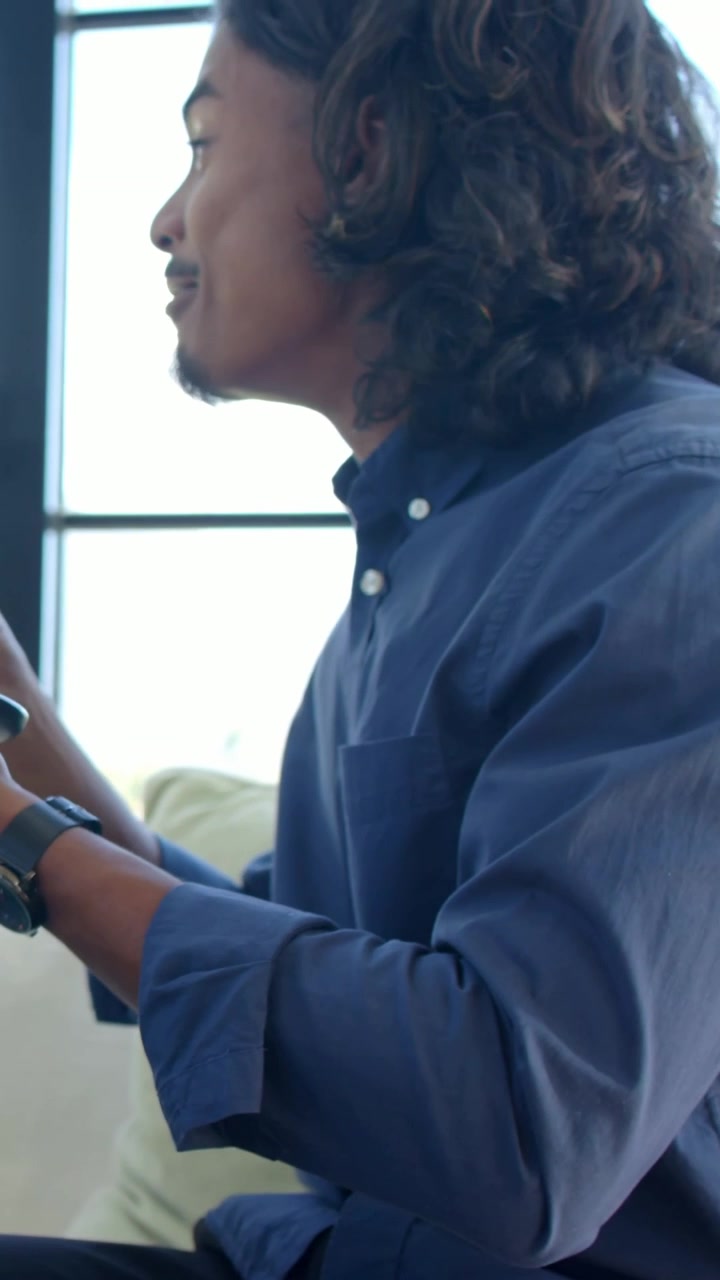 Vertical video: Moving camera, man in navy top holding tablet engaging guest near red drink at home