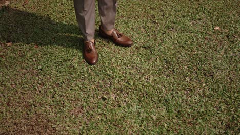 elegant brown dress shoes and formal trousers stride over trimmed lawn during outdoor event