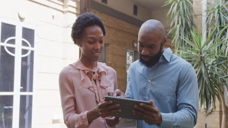 Two-african-american-male-and-female-colleagues-talking-and-using-tablet-outside,-in-slow-motion