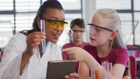 Diverse-female-teacher-and-schoolgirl-wearing-protective-glasses-with-test-tube-on-chemistry-class