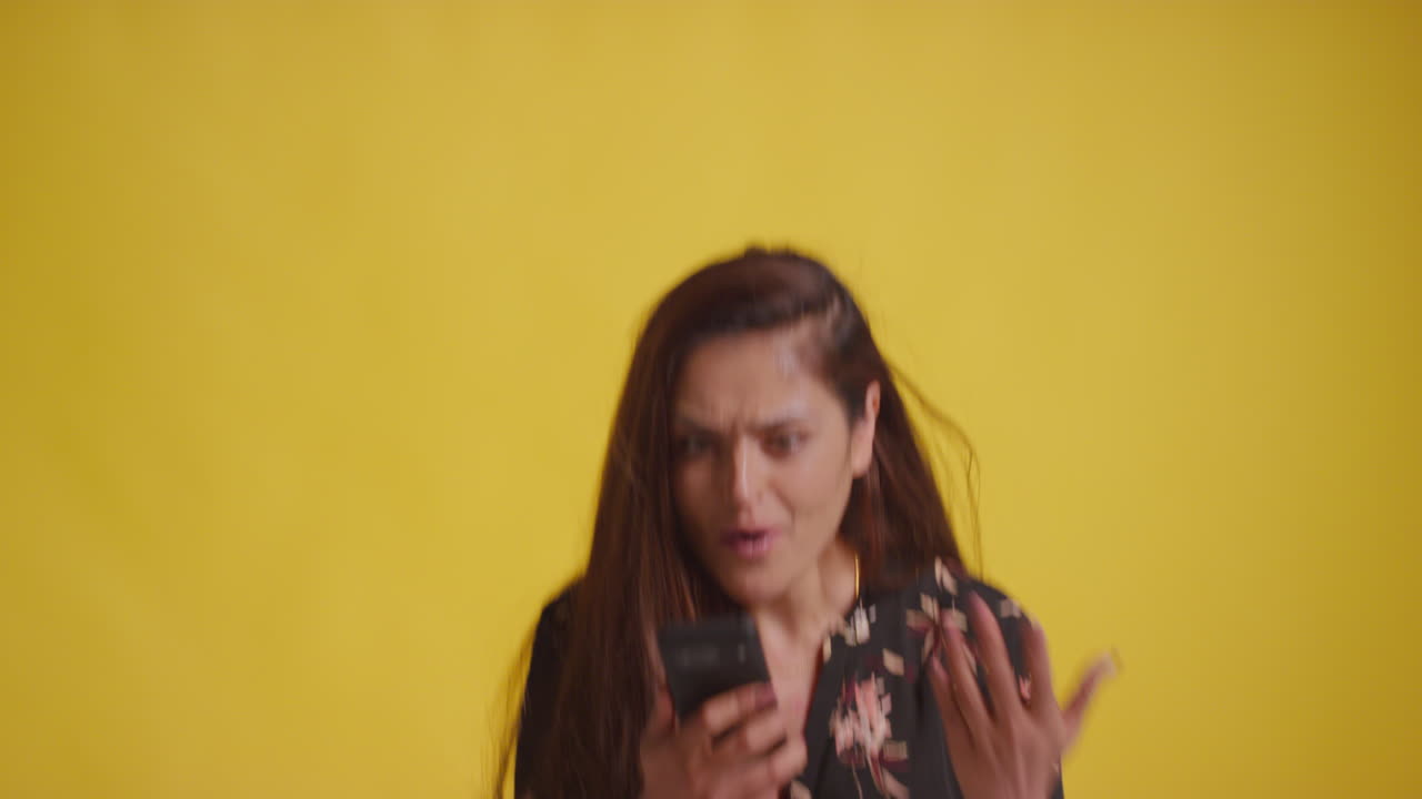 Studio Shot Of Excited Woman With Mobile Phone Celebrating Winning Money Against Yellow Background