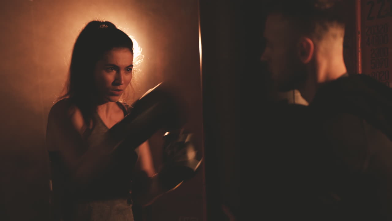 트레이너가 들고 있는 샌드백을 반복적으로 두드리는 여자 복서 열차